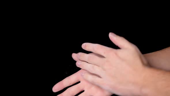 A person rubbing and dusting his hands with chalk powder, isolated on black background. Slow motion.