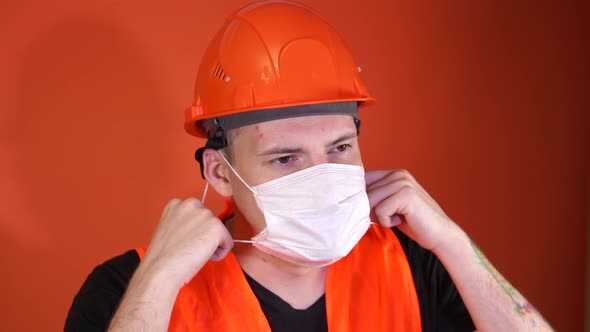 Male Construction Worker in Overalls Removing Medical Mask From Face on Orange Background