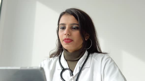 Indian Female Doctor in a White Coat with a Stethoscope Conducts an Online Consultation in Her