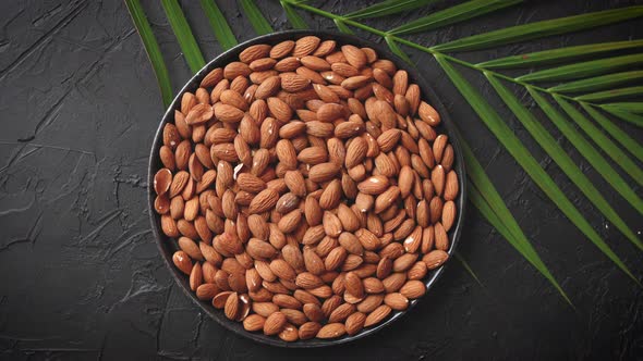 Composition of Whole Almond Nuts in Black Plate Placed on Black Stone Table