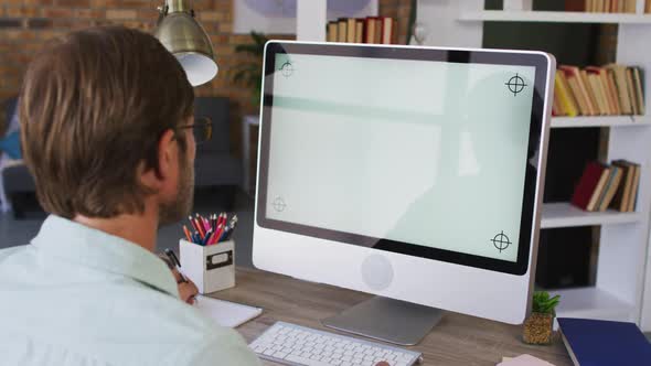 Caucasian male teacher taking notes while having a videocall on computer in the classroom at school