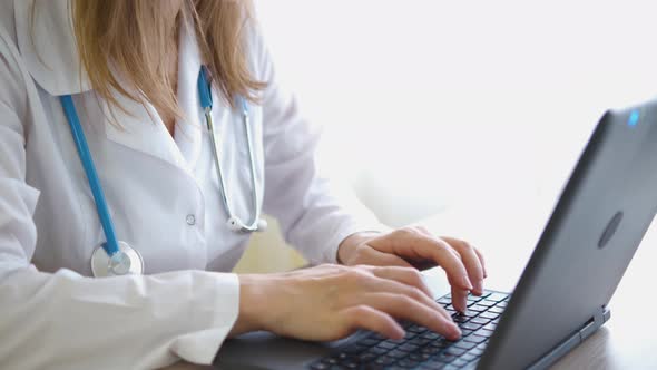 A girl in a white coat works on a laptop on the table close-up