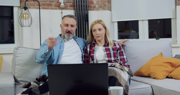 Woman Sitting Near Her Husband on Sofa and Does not Respond on His Revision Match on Laptop