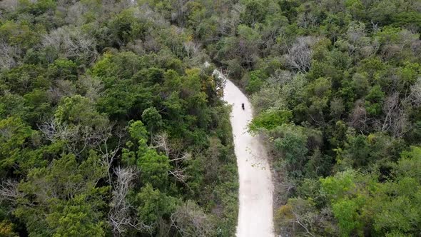 Aerial shot shot of motorbike driving in the dirt road surrounded by trees in Akumal Mexico. Modern