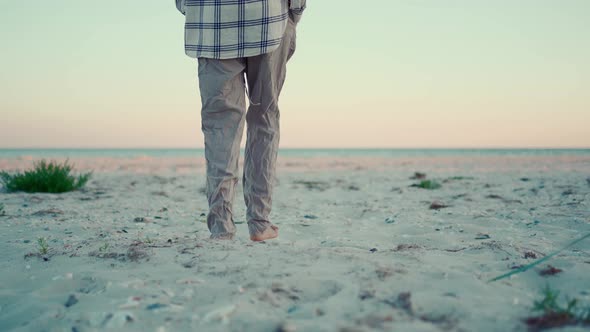 Woman Hipster Walks on Wild Sea Sand Beach at Sunset and Touches Spike of Grass By Hand