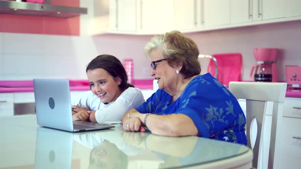 Positive girl teaching grandmother watching videos on laptop at home