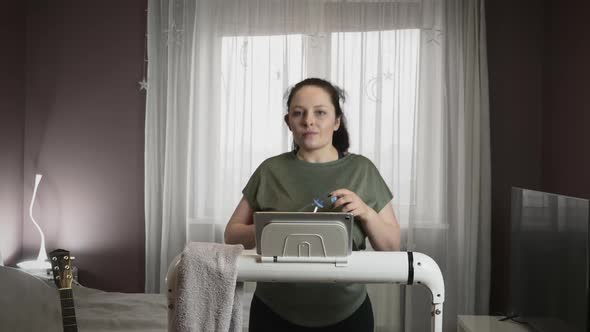 Woman is drinking water from bottle while walking on treadmill