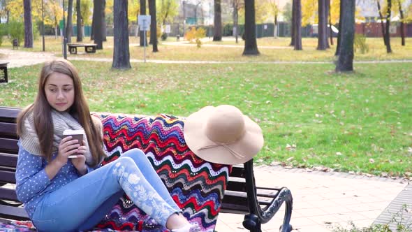 Beautiful Girl Sitting on a Bench in a Sunny Park in Autumn