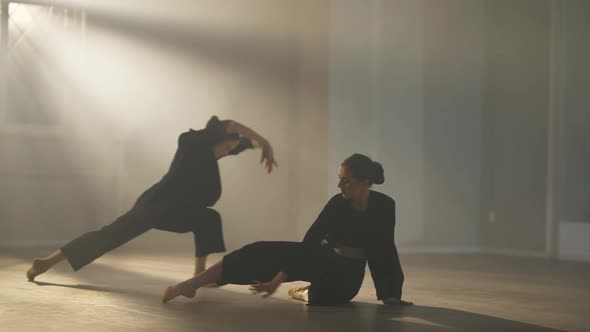 Two Flexible Graceful Slim Ballet Dancers Rehearsing in Backlit Fog in Studio Indoors