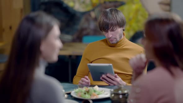 Absorbed Confident Caucasian Man Surfing Internet on Tablet As Blurred Women Talking at Front