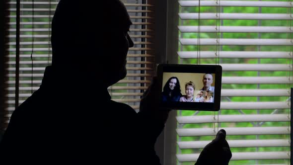 A Bald Man Is Facing the Light at a Window with Blinds, She Is Talking on a Video Conference on a