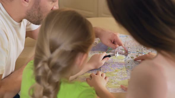 Excited Father, Mother and Daughter Looking at Map Through Magnifying Glass