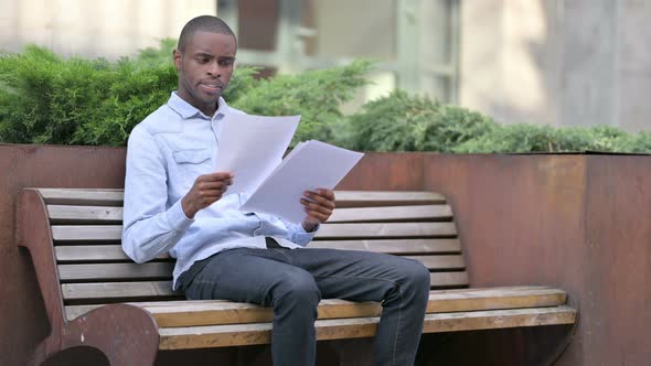 African Man Reading Documents Sitting Outdoor