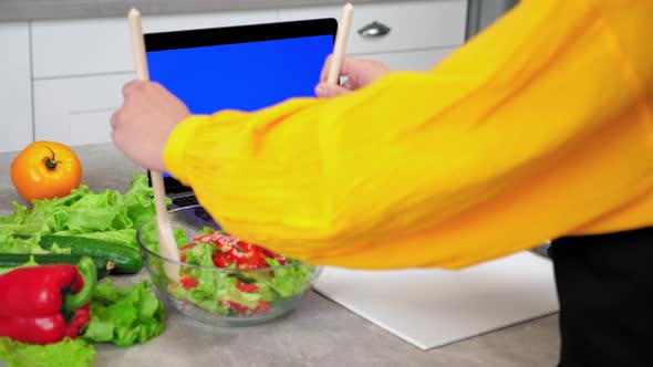 Woman in Kitchen Mixes Cooked Vegetarian Salad with Wooden Spoons in Glass Bowl