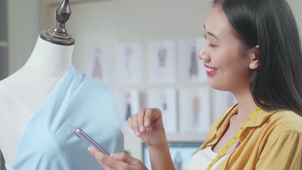 Female Designer Looking At A Dress On A Mannequin And Comparing It On Smartphone While Designing