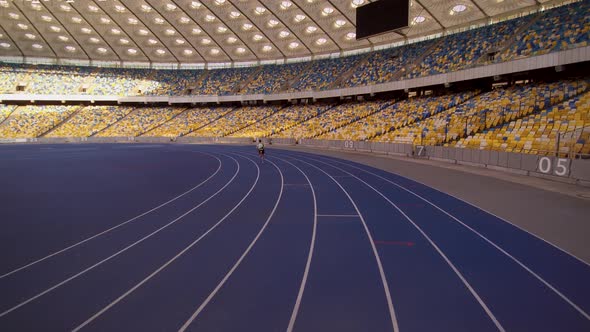 Athlete runs on long track around big empty stadium