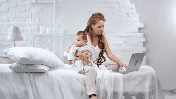 Multitasking Young Smiling Mother Chatting Using Laptop Pc Holding Cute Baby Enjoying Motherhood