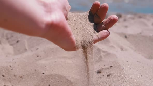 Female Hand Pours Sand Through Fingers on the Beach in the Rays of Sunlight