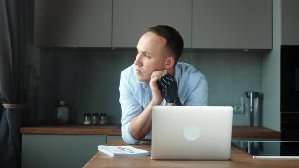 Freelancer man employee with bio hand prothesis sits at table with notes