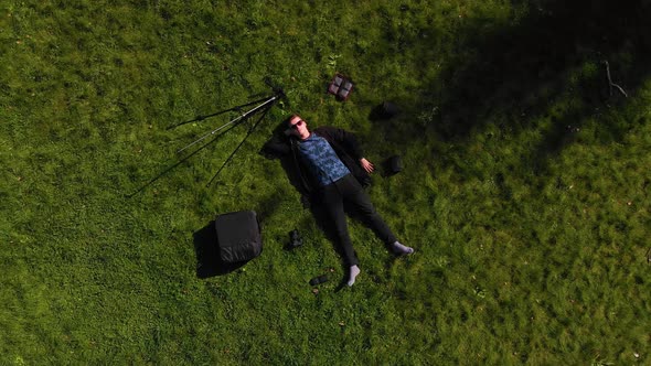 Person Lies Surrounded By Equipment on a Sunny Green Glade of the Park, the Camera Pulls Off