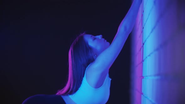 Young Woman Exercising in Neon Lighting  Bending Her Loin Against the Wall