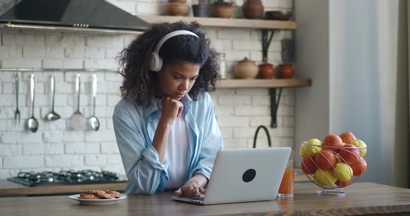 Female Freelancer in Headphones Working From Home on Kitchen and Using Laptop