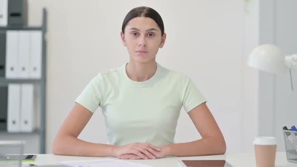 Serious Young Latin Woman Looking at Camera in Office