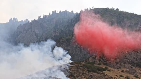 Small airplane dropping fire retardant on wildfire burning on mountainside