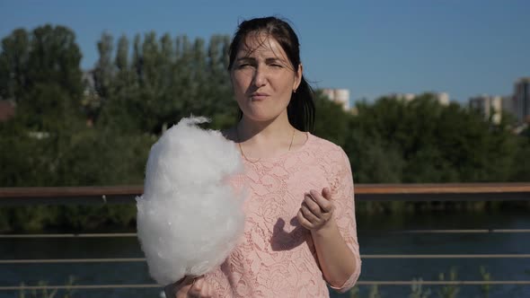 Young Woman Eating Sweet Cotton Wool Outdoors in Sunny Weather