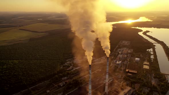 Manufacturing in nature at sunset. White smoke goes from metallurgical pipes into the air. 
