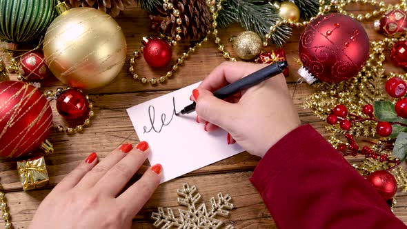 Woman's hand writing LET IT SNOW card near Christmas decorations