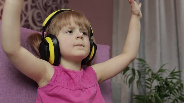 Little Child Girl in Headphones Enjoying Listen Music. Dancing on Sofa at Home