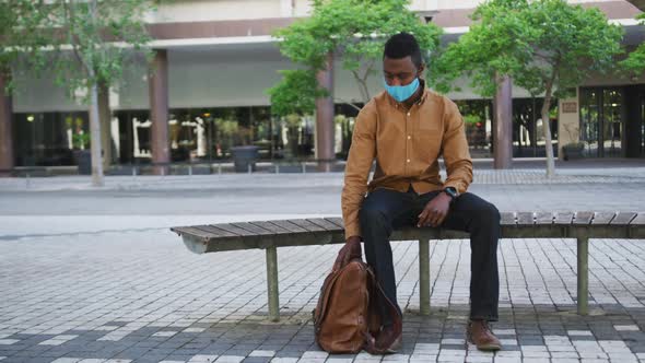 African american businessman wearing face mask sitting on bench