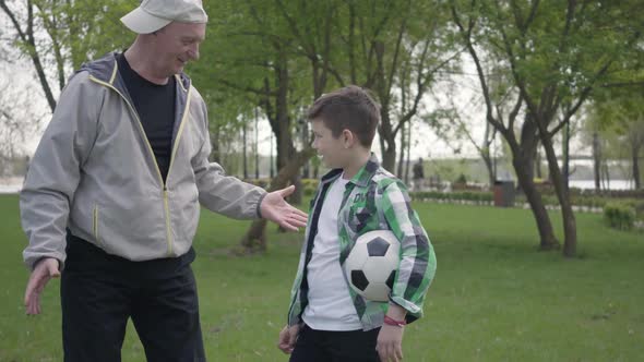 The Little Boy in a Checkered Shirt and Positive Old Man Finishing To Play Soccer in the Park