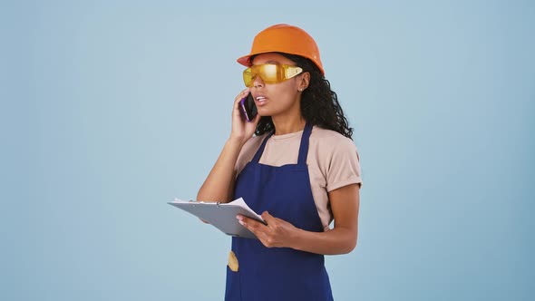 Darkskinned Woman Industrial Worker or Builder in Hard Hat and Protective Goggles is Talking By