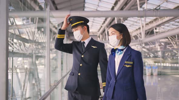 Airliner pilot and air hostess wearing face mask walking in airport terminal to the airplanel.