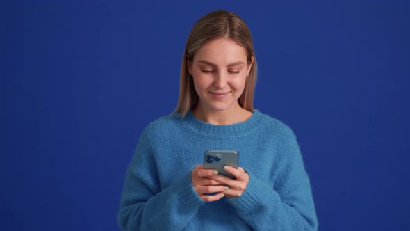 Positive woman wearing blue sweater texting by phone
