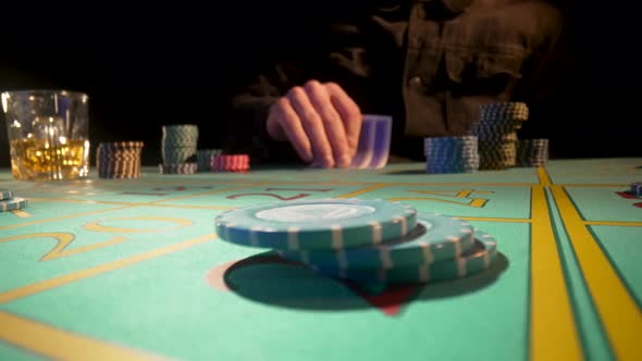 Unrecognizable Male Player Sits at Gaming Table in Casino and Drinks Whiskey From Glass