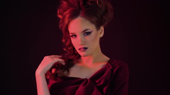 Portrait of a Young Beautiful Girl in a Red Dress, Enlightening in Red Light, She Is Posing Against