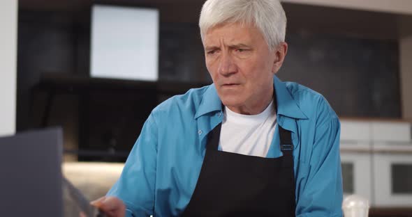 Senior Man Preparing Vegetarian Dinner Reading Recipe on Laptop