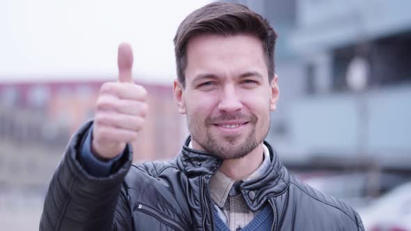 A Young Handsome Man Shows a Thumb Up To the Camera and Nods with a Smile in a Suburban Area