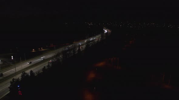 Cars driving at night on illuminated highway. Track left drone shot.