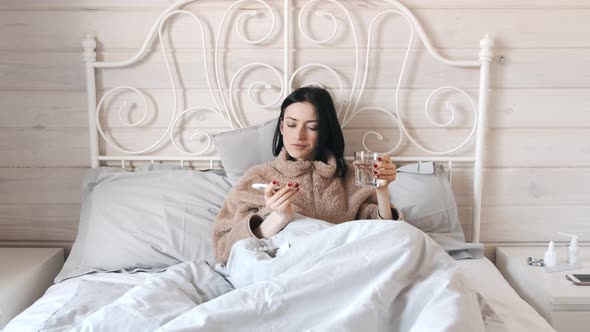 Sick Woman Laying in Bed and Taking in Pills