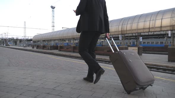 Unrecognizable Successful Businessman Walking Through Railway Station and Pulling Suitcase on Wheels