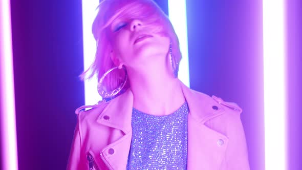 Fashionable Woman with Dyed Pink Hairstyle Dancing Relaxed in Room with Colorful Neon Glowing Lamps