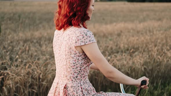 A Girl on a Bicycle is Riding a Field Road at Sunset