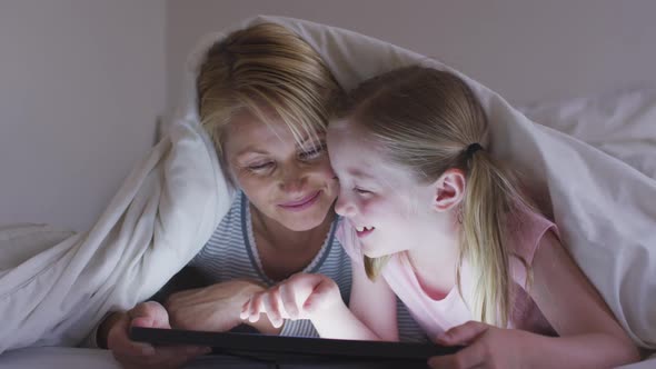 Front view of Caucasian woman and her daughter using digital tablet on bed