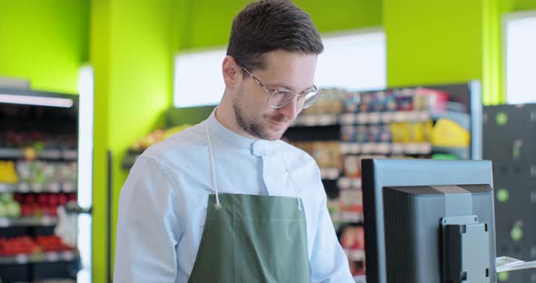 Man in Green Apron As a Cashier at the Cash Register in the Supermarket or Discounter