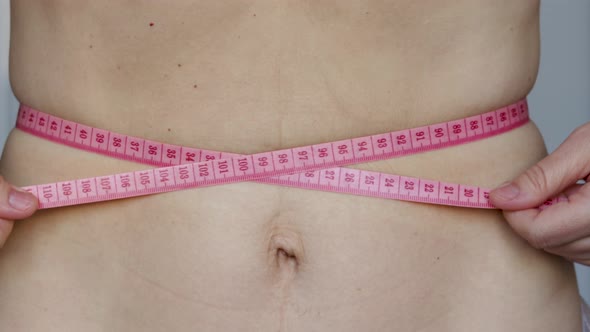 close up video of young woman tightening on her waist a pink color measure tape. diet and slim conce