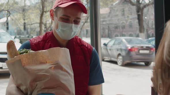 Postman or Delivery Man in Mask During Coronavirus Carry Small Box Food Deliver to Young Woman